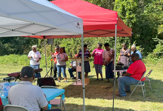 A group of people singing together under tents at an outdoor event.