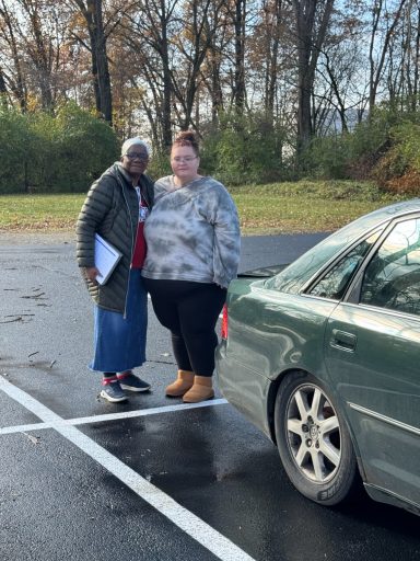 Two women standing together near a parked car in a parking lot.
