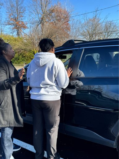 Two people interacting near a parked SUV on a sunny day.