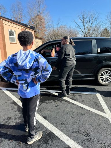 A child watches as an adult converses with someone in a parked black van.