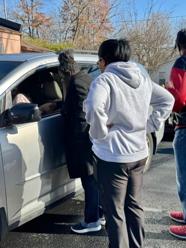 People interacting near a car in a parking lot on a sunny day.