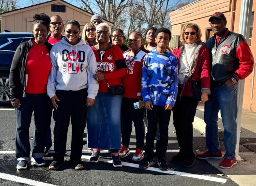 Group of people smiling together outdoors, wearing red and white attire.